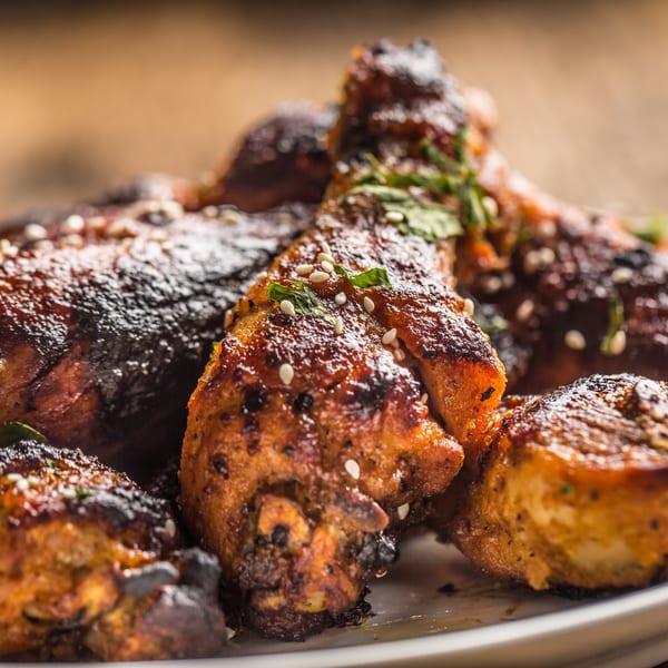 Close-up of several glistening Jahmakin Jerk n Juice chicken drumsticks, garnished with sesame seeds and herbs.